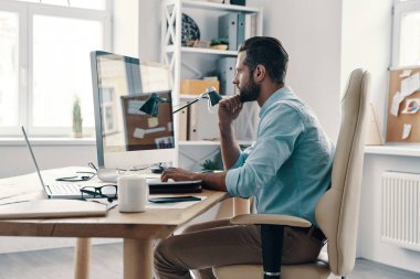 Genç ve modern iş adamı ofiste otururken bilgisayar kullanarak veri analiz ediyor.    