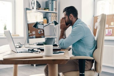 Tükenme. Ofiste otururken elleri yüz tutmak akıllı rahat giyim yorgun genç adam