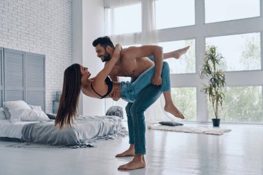Birlikte deli going, güzel genç çift kucaklayan ve yatak odasında dans ederken gülümseyen tam uzunlukta, adam kadın taşıyan 