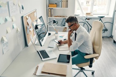 Ofiste otururken akıllı telefon kullanarak ve gülümseyerek gömlek ve kravat iyi görünümlü genç adam üst görünümü             