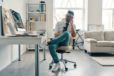 Ofiste otururken akıllı telefon kullanarak ve gülümseyen gömlek ve kravat iyi görünümlü genç adam               
