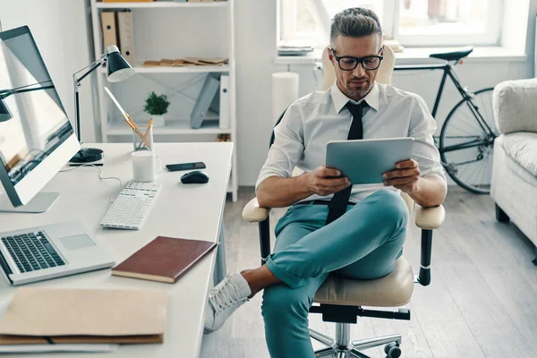 商人在衬衫和领带使用数字平板电脑和微笑 而坐在办公室扶手椅与自行车的背景 — 图库照片
