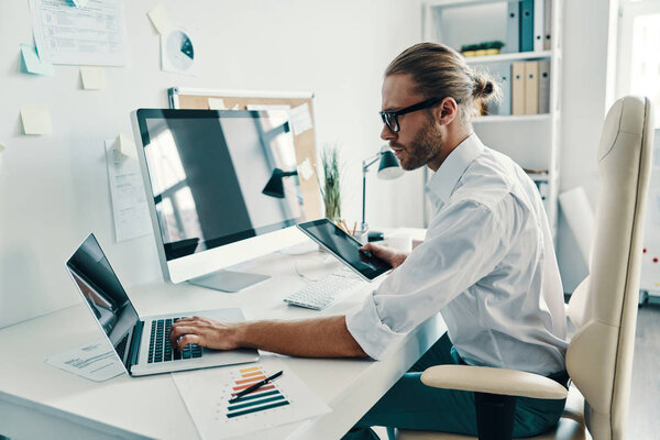 Good looking young man in shirt using digital tablet while sitting in the office         