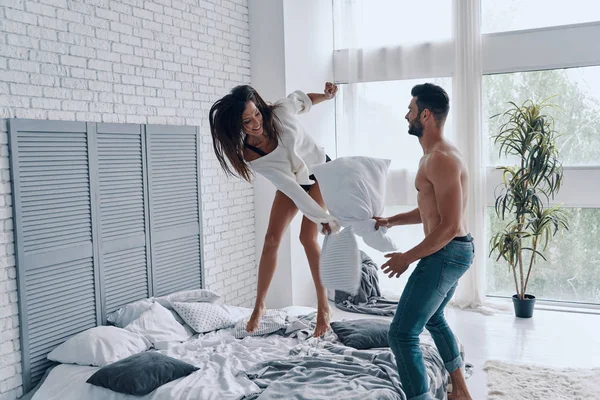 快乐的年轻夫妇有一个有趣的枕头战斗 而花无忧无虑的时间在卧室 — 图库照片