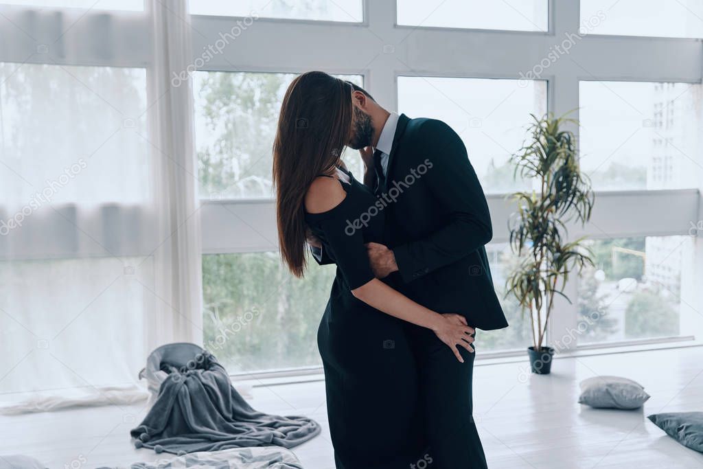 Beautiful young couple kissing and embracing while standing time in the bedroom