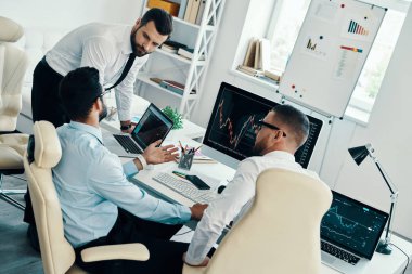 Ofiste çalışırken borsa verilerini analiz formalgiyim genç modern erkek grubu               