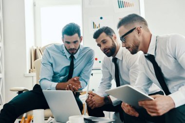 Ofiste otururken dizüstü bilgisayar kullanarak çalışan formalgiyim genç modern erkek grubu