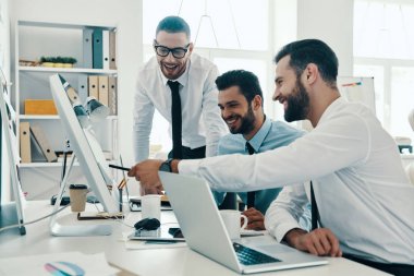 Doğru kararı arayan, ofiste otururken bilgisayar kullanarak çalışan formalgiyim genç modern erkek grubu       