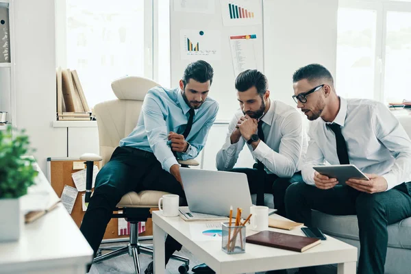 オフィスに座っている間 技術を使って働くフォーマルウェアの若い現代男性のグループ — ストック写真