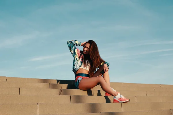 屋外の階段に座りながら笑顔のスポーツ服を着た魅力的な若い女性 — ストック写真