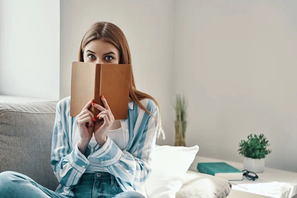 Jovem Atraente Olhando Para Câmera Cobrindo Rosto Com Livro Enquanto — Fotografia de Stock