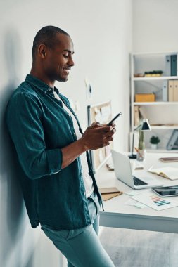 Mutlu bir iş adamı. Ofiste dururken akıllı telefon kullanarak gömlek yakışıklı genç Afrikalı adam