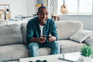 Çok eğlenceli! Yakışıklı genç Afrikalı adam video oyunu oynarken ve kapalı otururken gülümseyerek