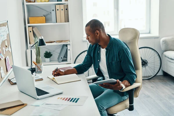 クリエイティブなビジネスマン シャツを着た思慮深いアフリカ人男性がオフィスに座っている間に何かを書き留めた — ストック写真