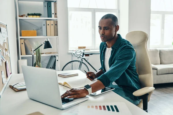 忙碌的工作日 深思熟虑的非洲青年穿着衬衫 坐在办公室时使用笔记本电脑 — 图库照片