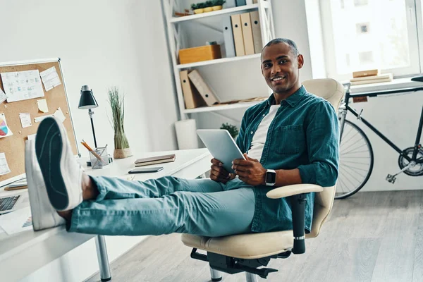 自信的经理 英俊的年轻非洲男子在衬衫看着相机和微笑 而坐在办公室 — 图库照片
