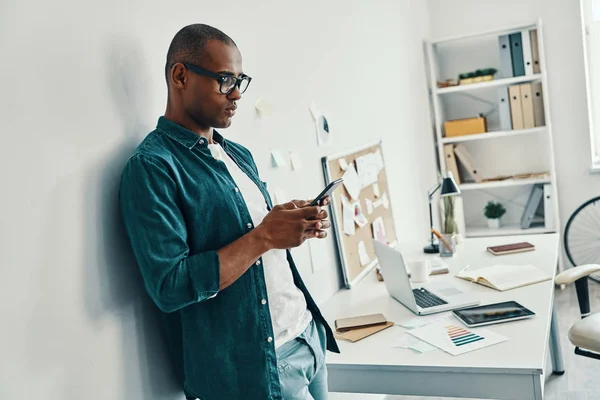 生意就是他的生命 英俊的年轻非洲男子在衬衫使用智能手机 而站在办公室 — 图库照片