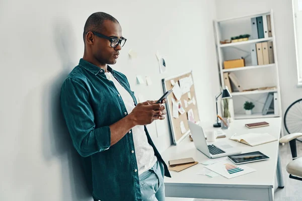 İş onun hayatı. Ofiste dururken akıllı telefon kullanarak gömlek yakışıklı genç Afrikalı adam