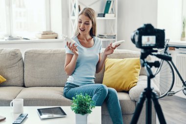 Güzel genç kadın gülümseyerek ve evde sosyal medya video yaparken güzellik ürünleri gösteren