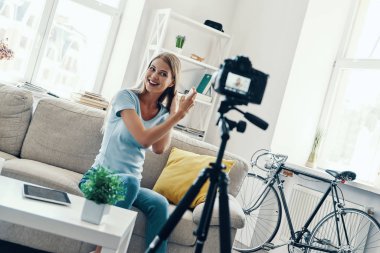 Güzel genç kadın gülümseyerek ve evde sosyal medya video yaparken saçlarına güzellik ürünleri uygulayarak