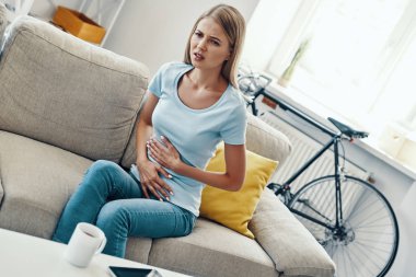 Genç kadın evde kanepede otururken mide ağrısı dokunmadan ve bir yüz yapma