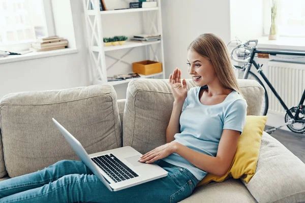 Güzel genç kadın gülümseyen ve evde kanepeüzerinde dinlenirken dizüstü bilgisayar kullanarak