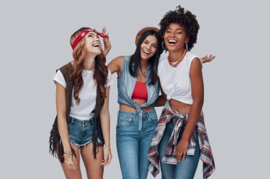 Gri arka planda dururken gülen üç çekici şık genç kadın