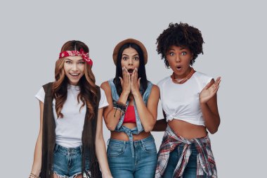 Üç şok genç kadın kameraya bakarak ve gri arka plan karşısında dururken bir yüz yapma