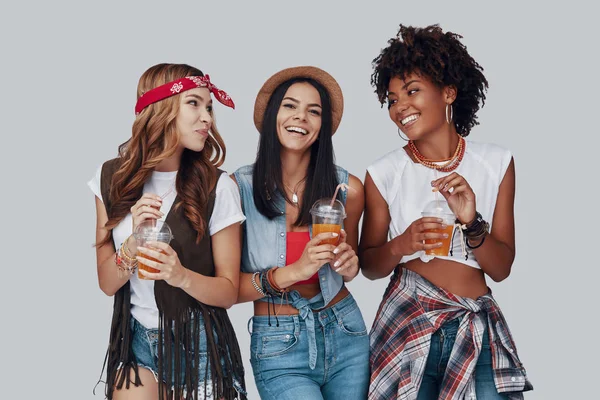 三个迷人的年轻女性喝着清爽的鸡尾酒 面带微笑 站在灰色背景上 — 图库照片