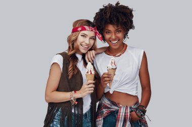 İki çekici genç kadın kameraya bakıyor ve gri arka plan karşısında dondurma yerken gülümsüyor 