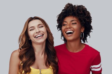 Two attractive young women smiling while standing against grey background clipart