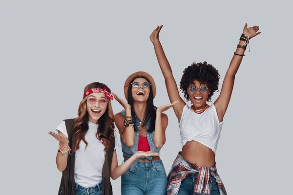 Three attractive young women cheering and smiling while standing against grey background