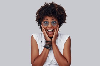 kameraya bakarak ve gri arka plan karşı dururken gülümseyen sürpriz genç Afrikalı kadın