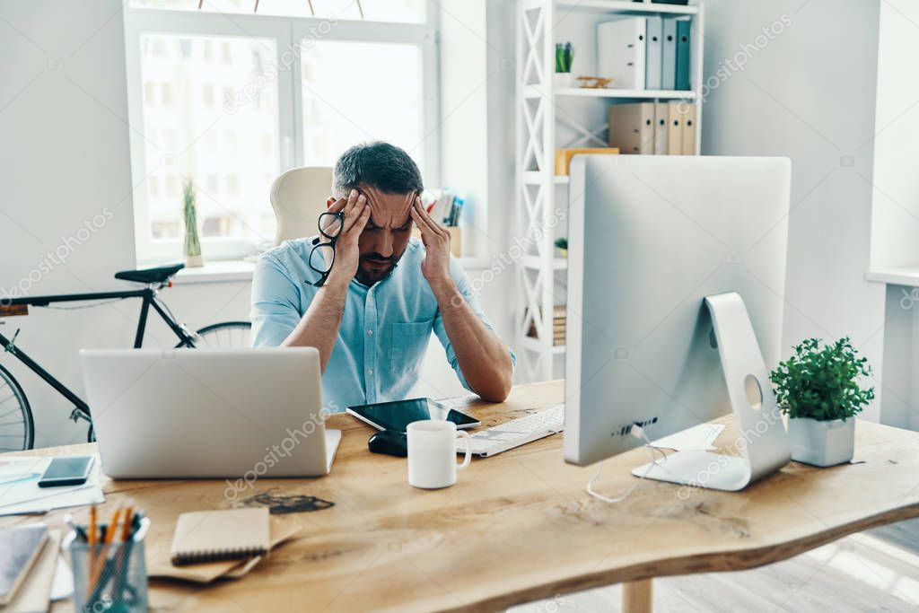 Frustrated middle age man in smart casual wear keeping head in hands while sitting in the office