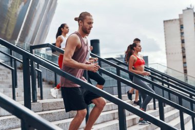 Spor giyimli bir grup genç dışarıda merdivenlerde egzersiz yaparken koşu yapıyor                