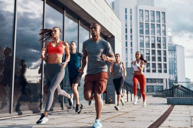 Group of people in sports clothing jogging while exercising on the sidewalk outdoors        clipart