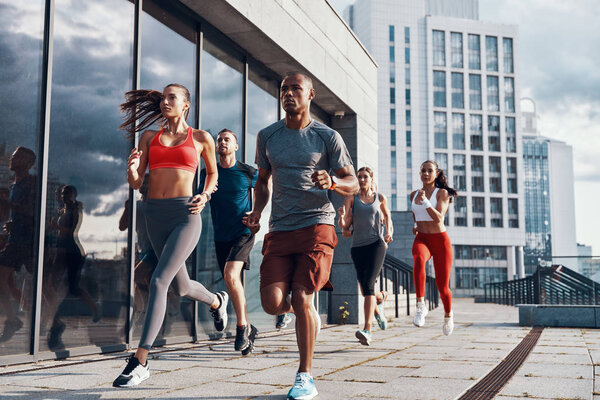 Group of people in sports clothing jogging while exercising on the sidewalk outdoors       