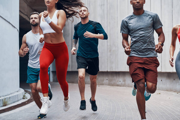Group of young people in sports clothing jogging while exercising outdoors 