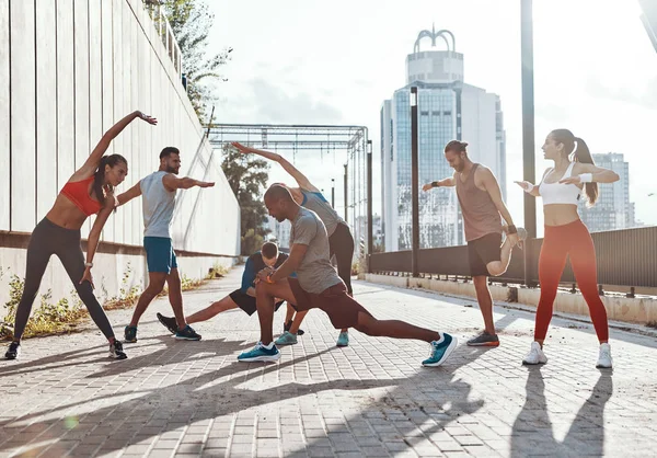屋外の歩道で運動しながら スポーツウェアの人々の完全な長さウォーミングアップとストレッチ — ストック写真
