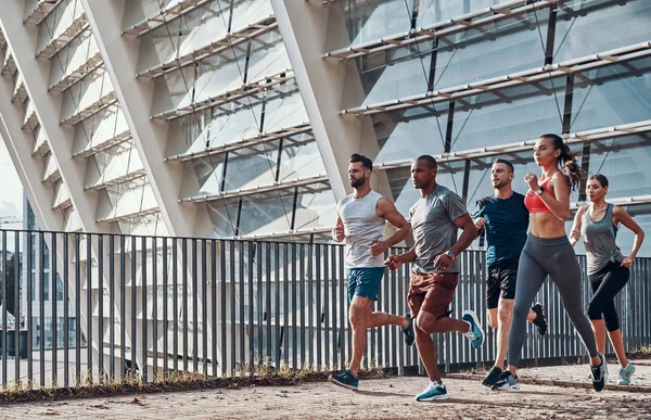 一群穿着运动服的年轻人在奥林匹克体育场大楼的城市慢跑 — 图库照片