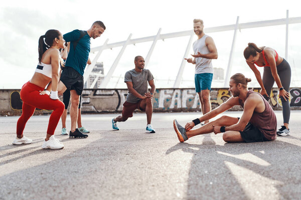 Full length of people in sports clothing warming up and stretching while exercising outdoors 
