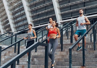 Merdivenlerde şehirde koşu gösteren sportif bir grup, arka planda Olimpiyat stadyumu 