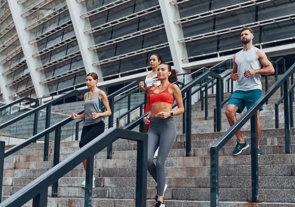 Merdivenlerde şehirde koşu gösteren sportif bir grup, arka planda Olimpiyat stadyumu 