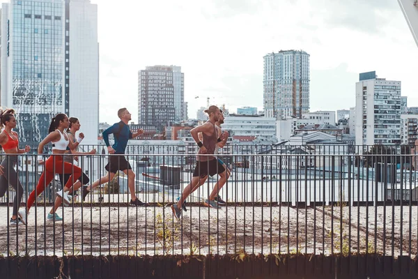 friends in sports clothing jogging on bridge outdoors in city with buildings and houses