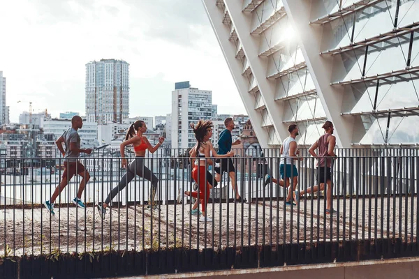 friends in sports clothing jogging on bridge outdoors in city with buildings and houses