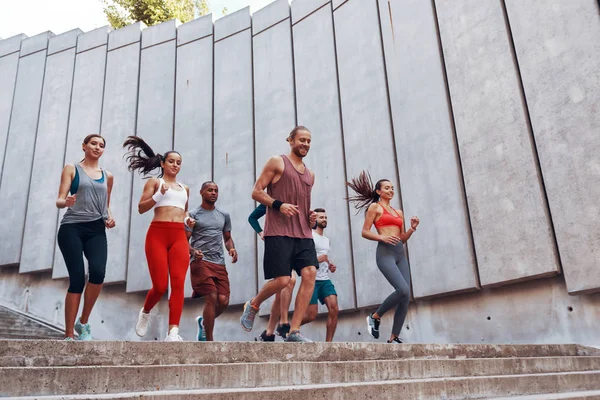 Group of sportive people jogging in city on stairs at big concrete wall