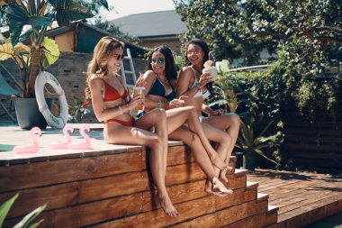 içecekler kokteyller ile ahşap havuz başında oturan mayo bikini gülen genç kadınlar