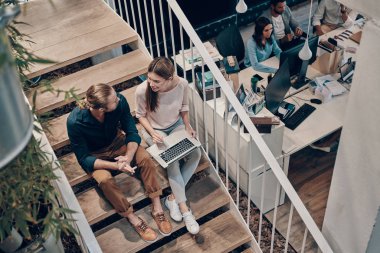 Akıllı gündelik giyim iki genç modern meslektaşlarının üst görünümü iletişim ve merdivenlerde otururken dizüstü bilgisayar kullanarak