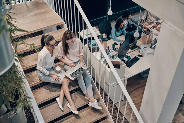 スマートカジュアルウェアの2人の若い現代女性のトップビューは 階段に座っている間 通信し ラップトップを使用しています — ストック写真
