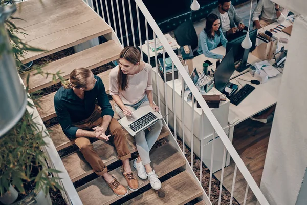 Akıllı gündelik giyim iki genç modern meslektaşlarının üst görünümü iletişim ve merdivenlerde otururken dizüstü bilgisayar kullanarak
